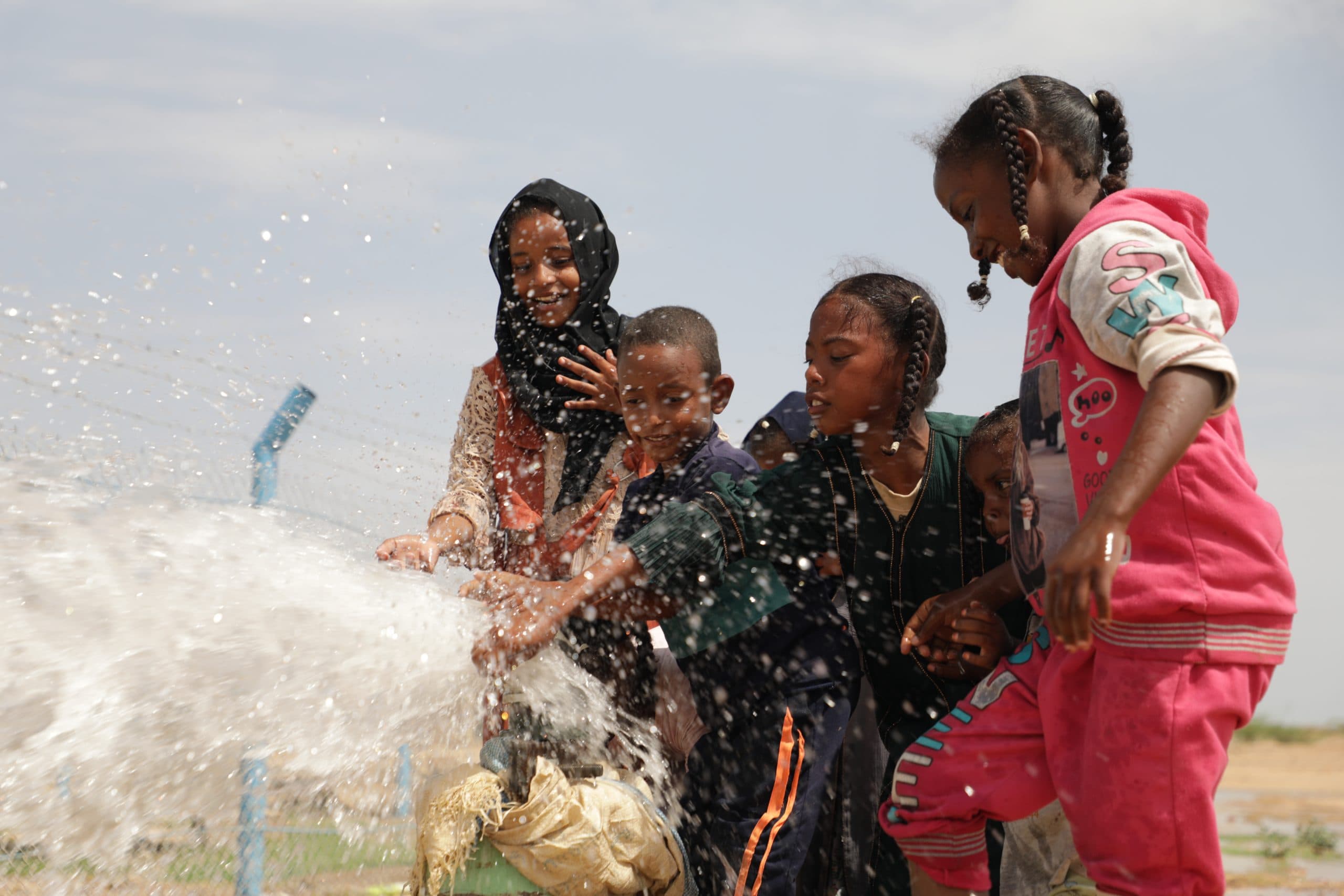 Children beside flowing water at Sadagaat’s Al Nabti Water Station.